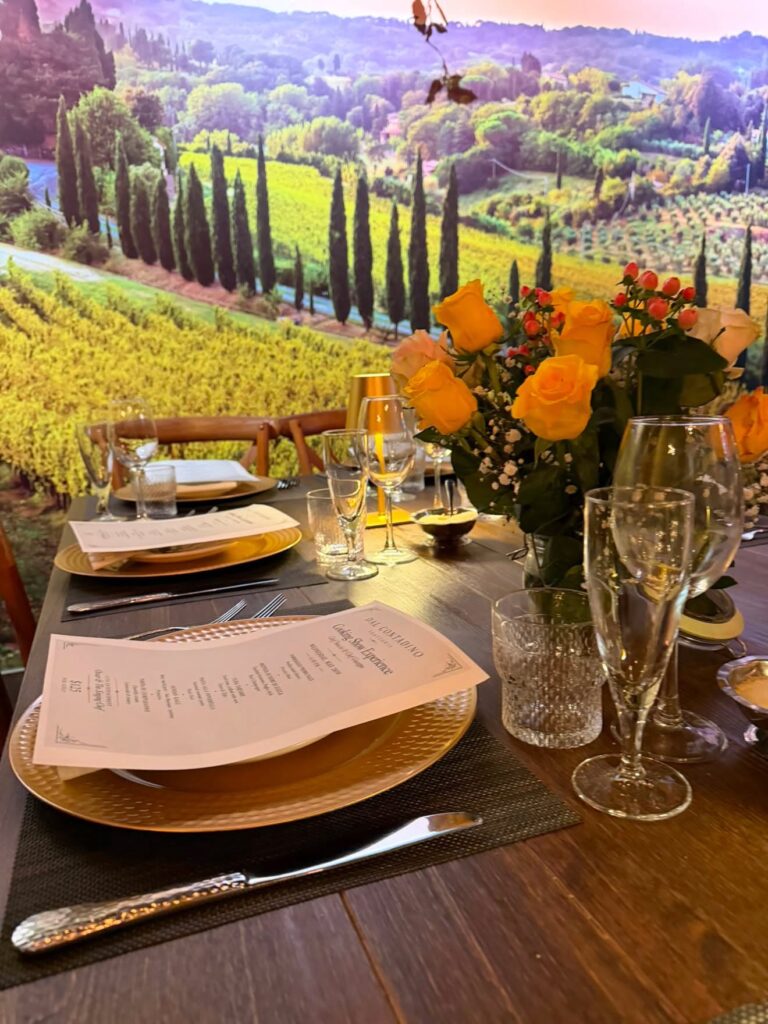 Tuscan Room private dining table set with gold chargers, menus and yellow roses in front of a vineyard mural at Contadino